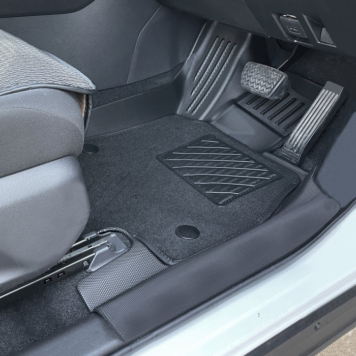 Driver-side footwell with custom-fit floor mat, textured heel pad, and raised edge design for enhanced grip and pedal area protection.